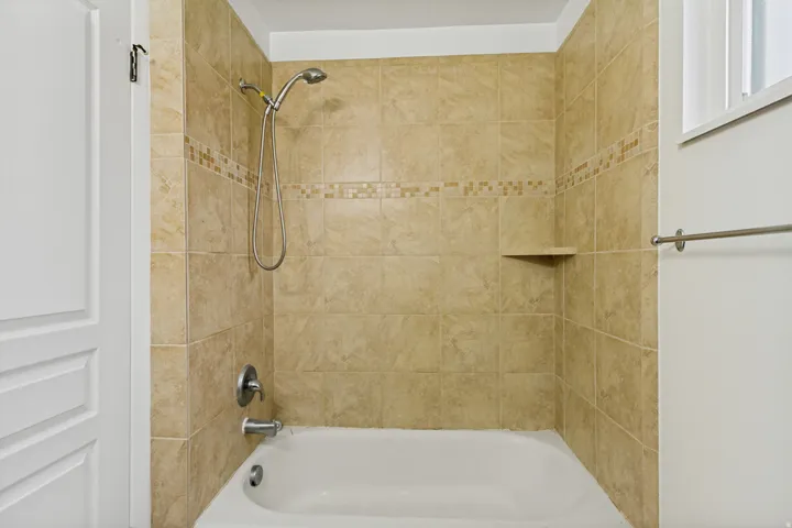 Bathtub and shower combination featuring neutral-toned tile surround with decorative mosaic accent band