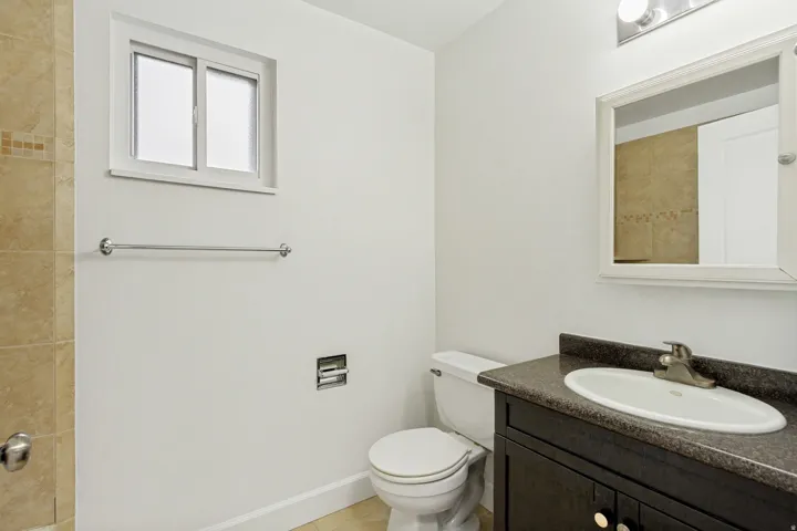 Bathroom featuring a dark wood-finish vanity with an integrated sink, a framed mirror, and a window with privacy glass