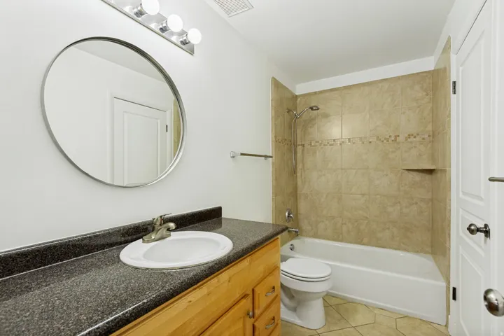 Bathroom featuring a wood-finish vanity with a dark speckled countertop, an oval mirror, and a four-bulb vanity light fixture