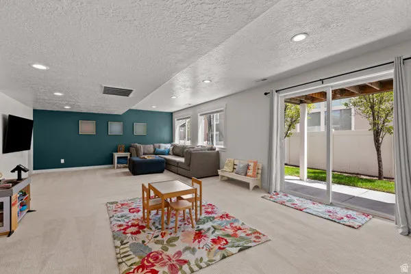 Spacious living area featuring a direct access sliding glass door, recessed lighting, a contrasting accent wall, multiple windows, and light-toned carpeting