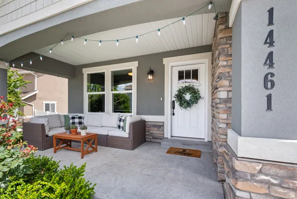 Covered front porch featuring a white entry door with upper window panes, stone veneer accents, and exterior wall sconce