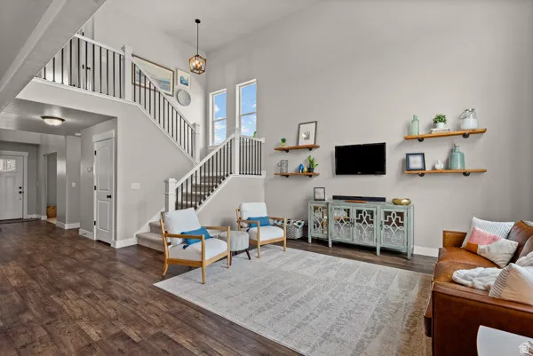 Spacious living area featuring high vaulted ceilings, wood-finish flooring, and a grand staircase with wrought iron balusters