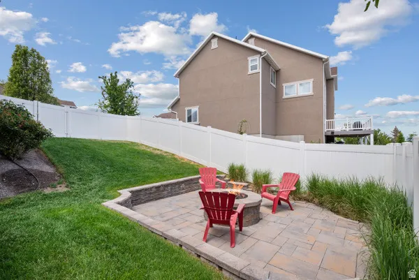 Backyard patio featuring paver stones, a built-in stone fire pit, a tiered retaining wall, and mature landscaping