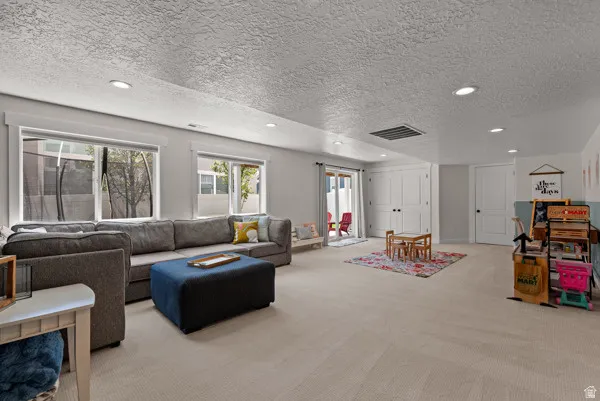 Spacious interior room featuring light-colored carpeting, recessed lighting, and multiple windows