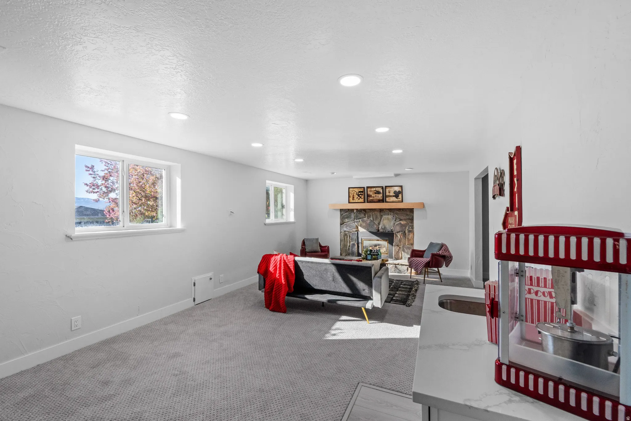 Spacious recreation room featuring recessed lighting, gray carpeting, and a stone-faced fireplace with a wood mantel