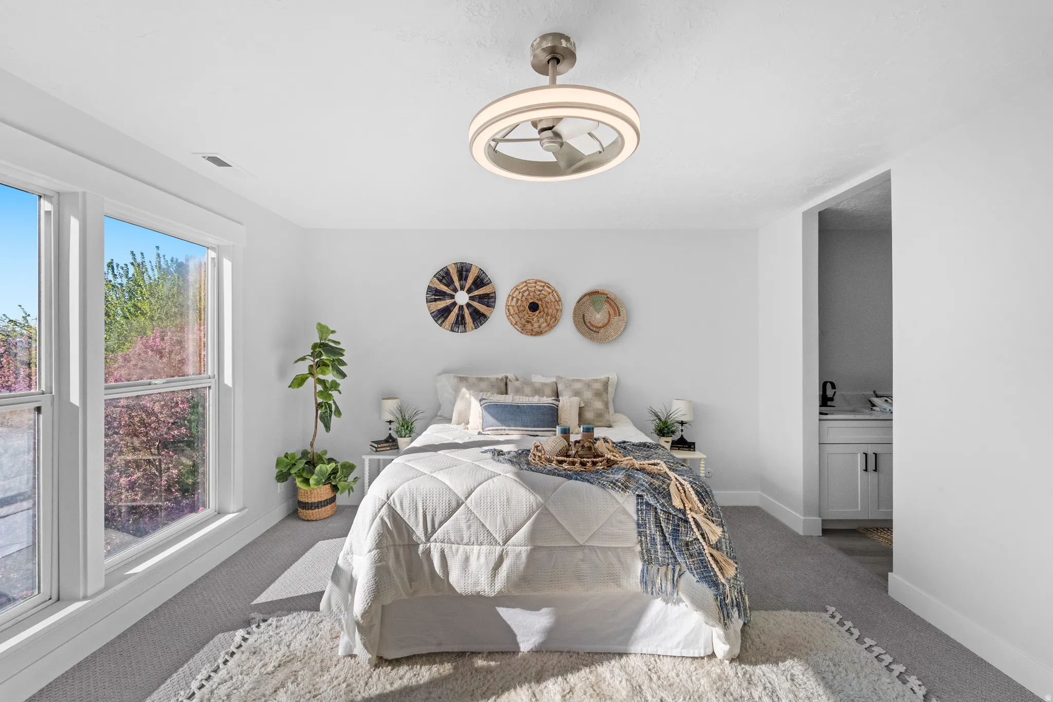 Bright bedroom featuring two large windows, a modern ceiling fan with integrated lighting, and neutral carpeting
