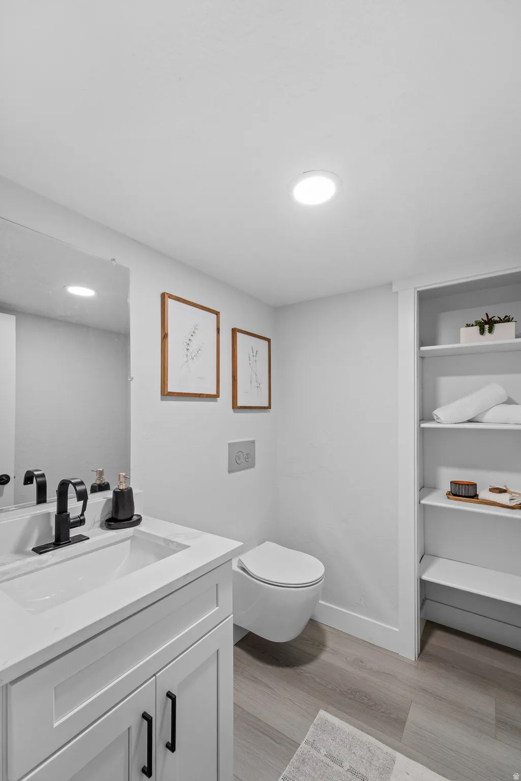 Bathroom featuring a white vanity with integrated sink, black fixtures, and a wall-mounted toilet