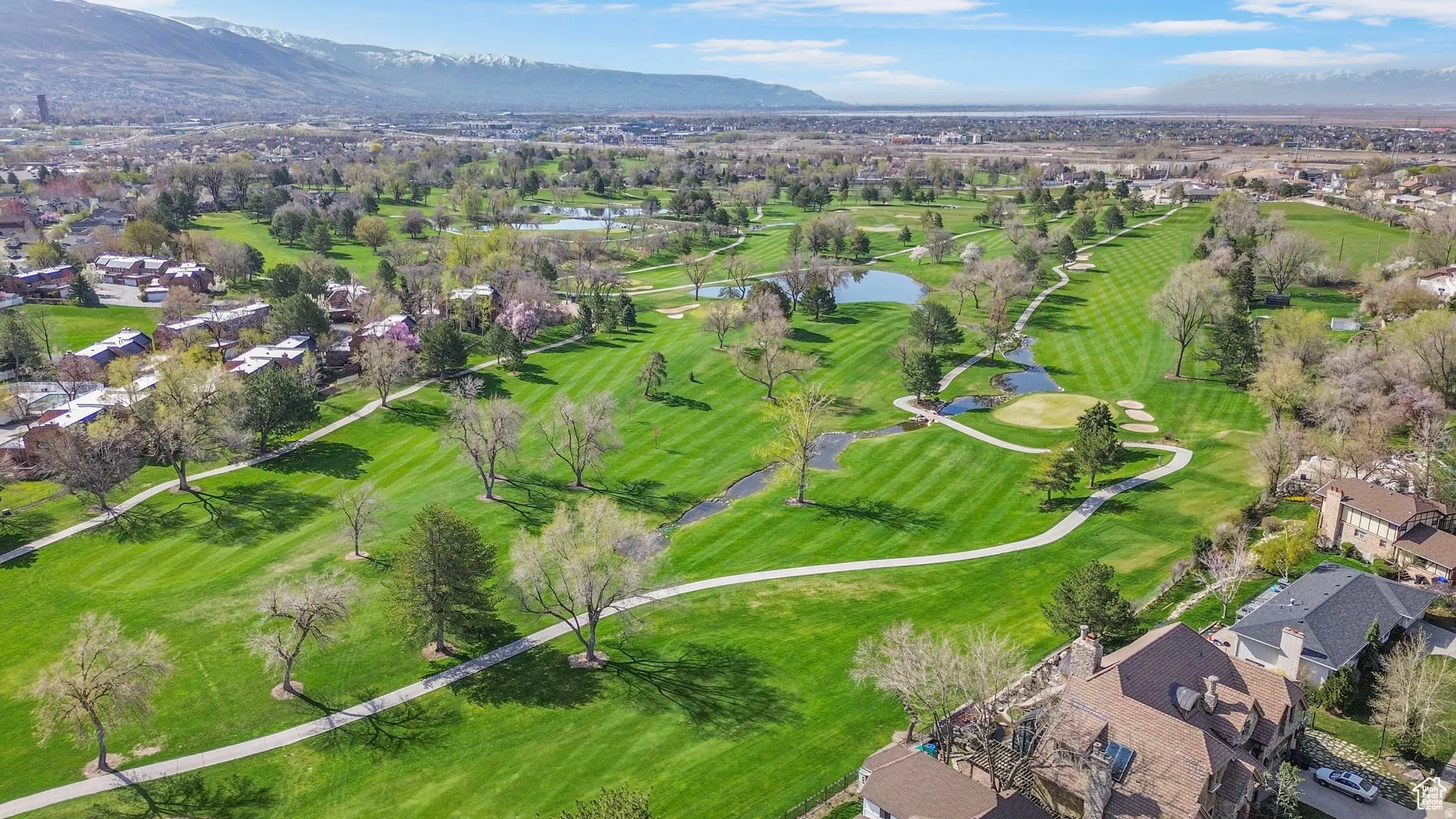 Expansive golf course setting featuring manicured fairways, mature trees, multiple water features, and mountain backdrops