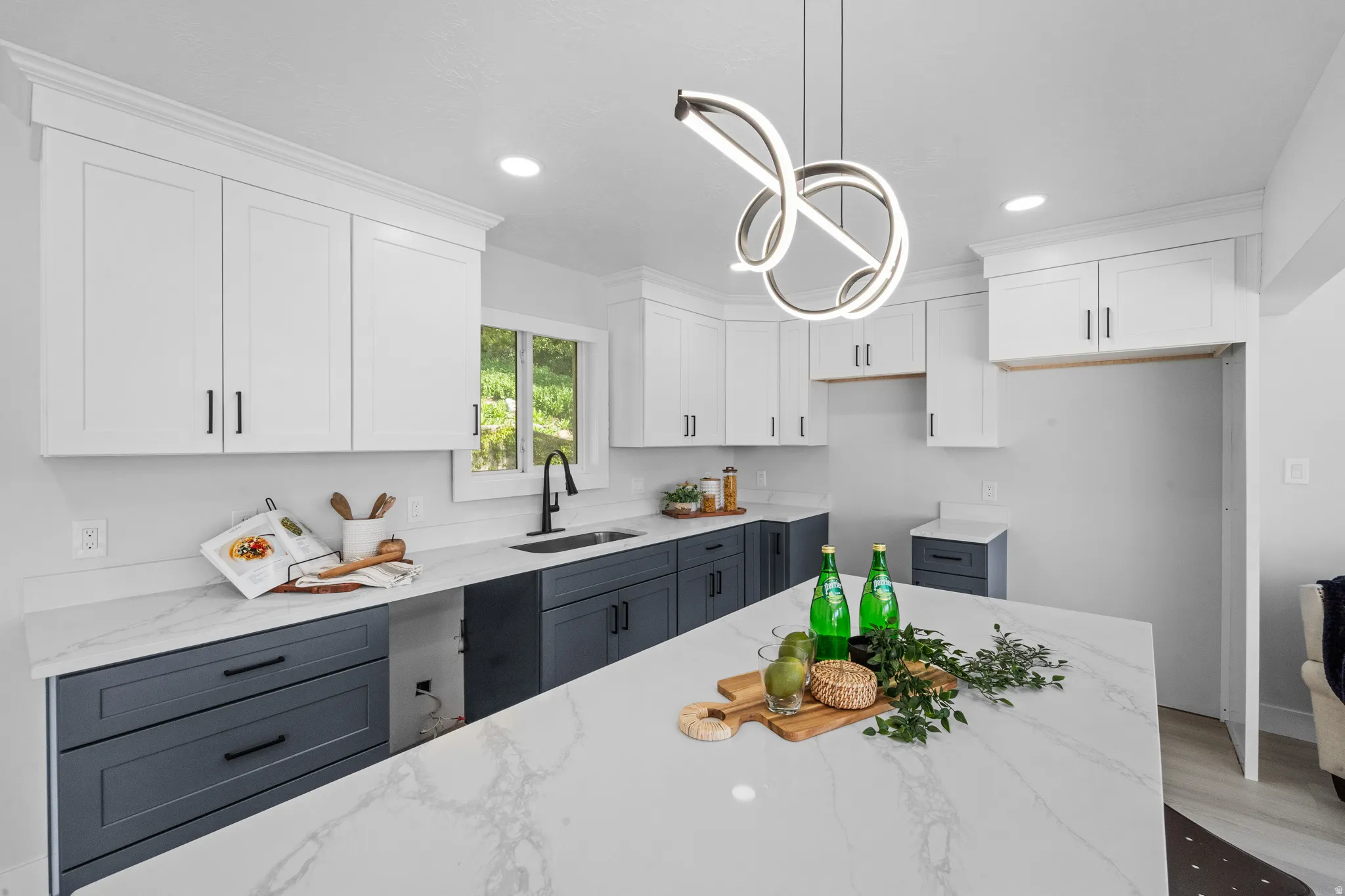 Contemporary kitchen featuring a large central island with a waterfall edge, white shaker-style upper cabinetry, dark base cabinetry, quartz countertops, and a modern pendant light fixture