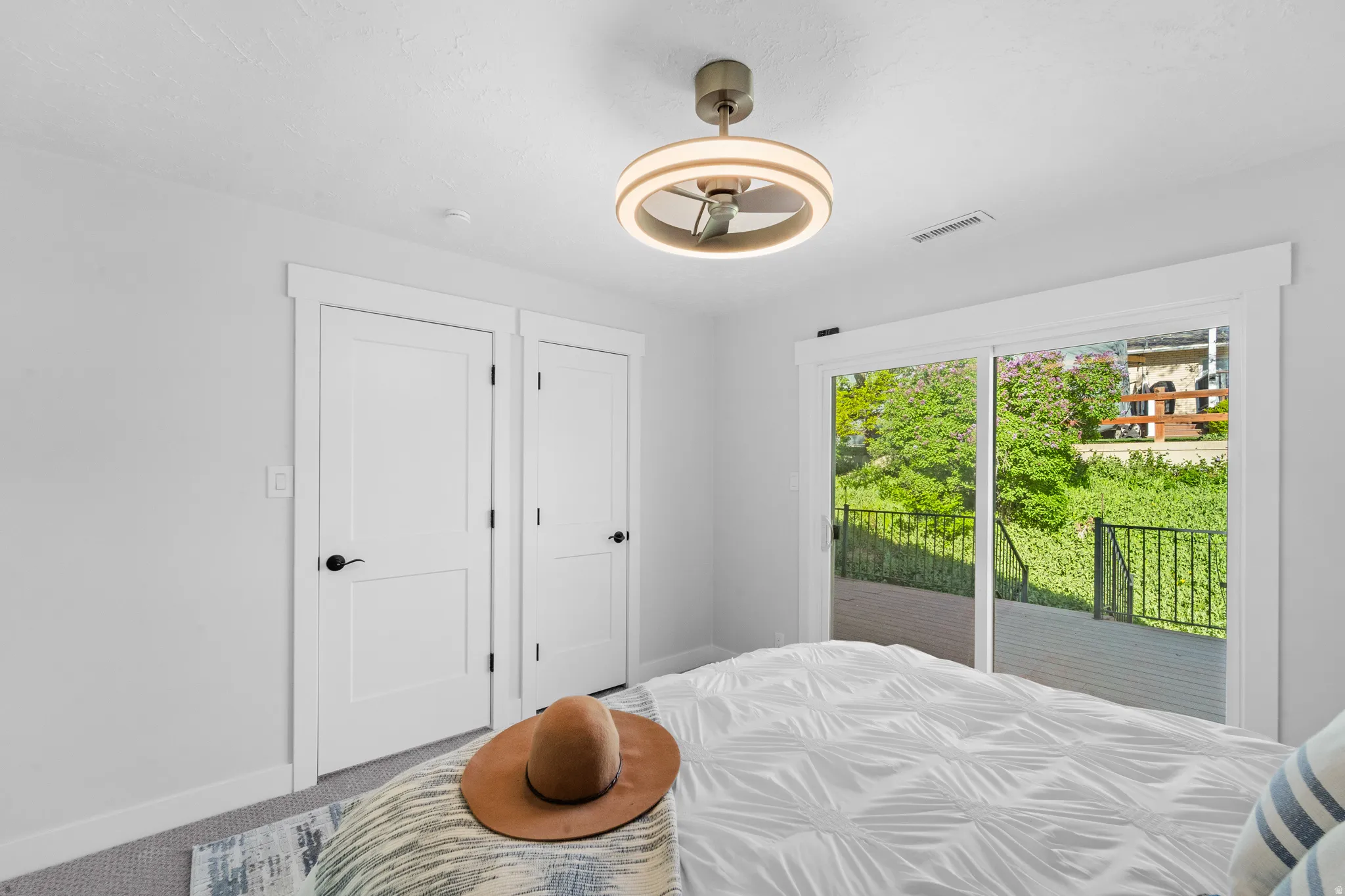 Sliding glass door opening to a private deck with black metal railing, offering lush green outdoor scenery