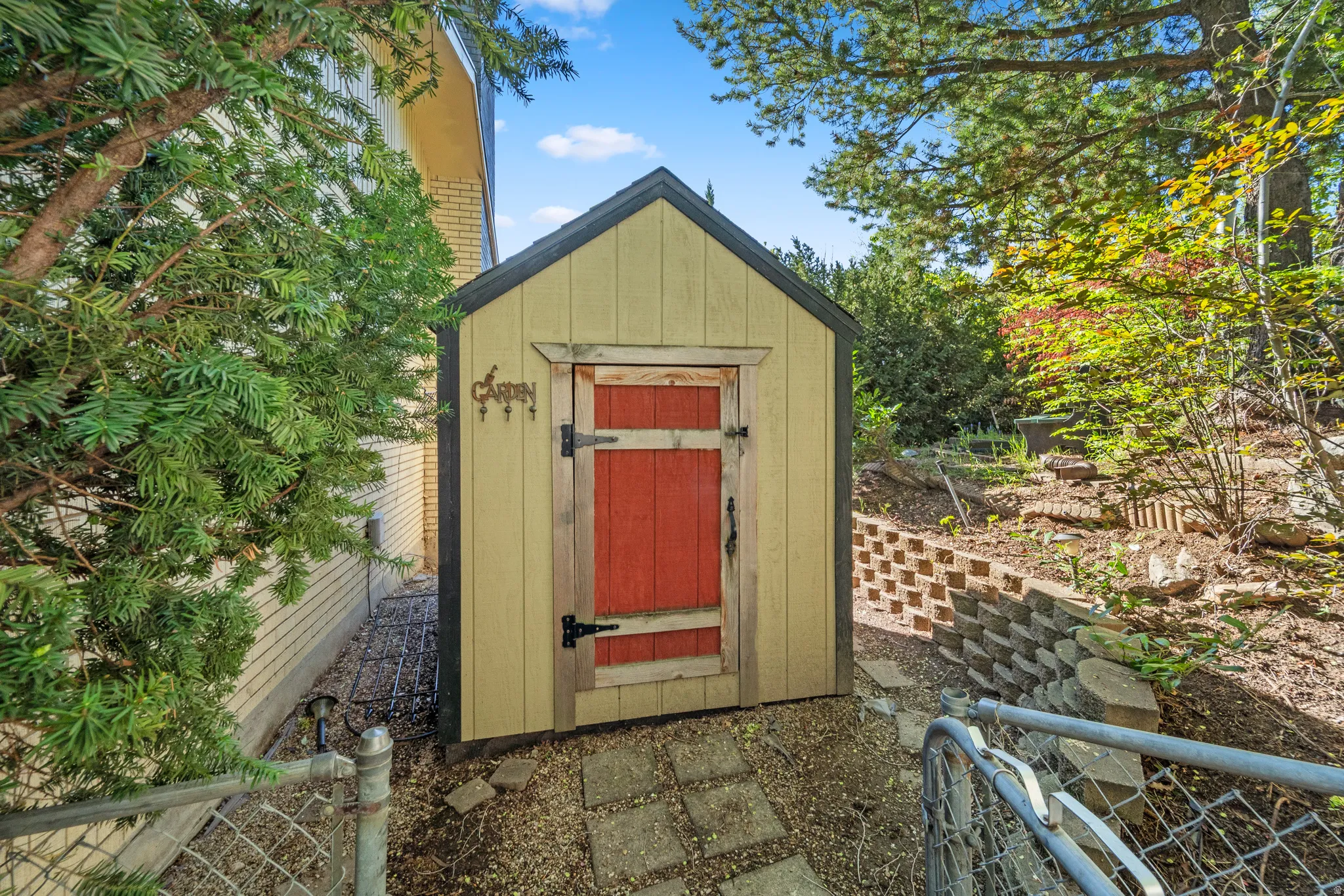 Gabled storage shed with a vibrant red door, featuring a shingle roof and light-colored siding