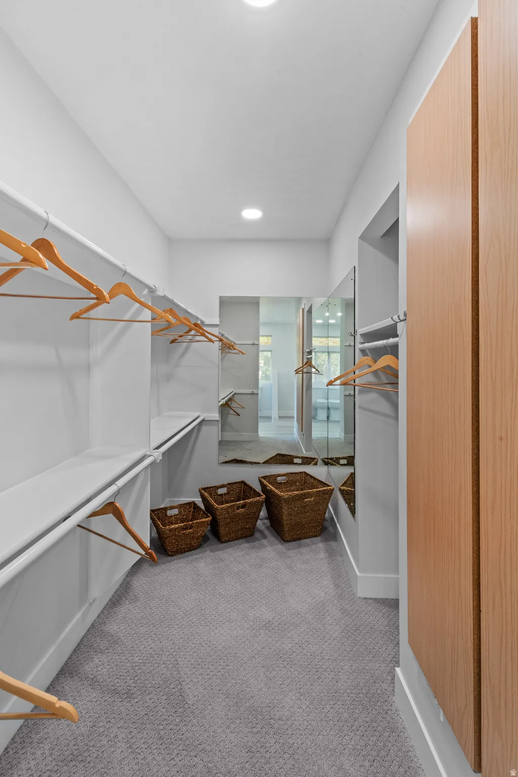 Walk-in closet featuring extensive built-in shelving, hanging rods, recessed ceiling lighting, and light wood-finish cabinetry
