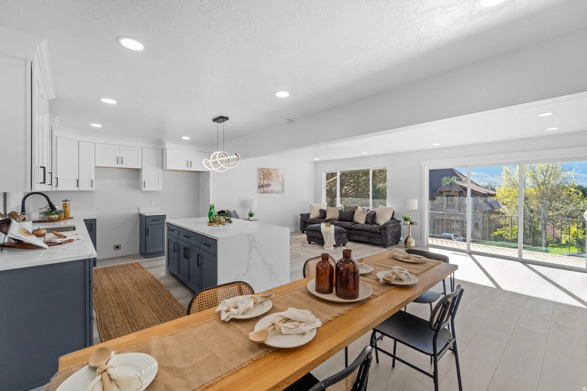 Open-concept living space featuring a kitchen with white upper and blue lower cabinetry, a waterfall island, and recessed lighting