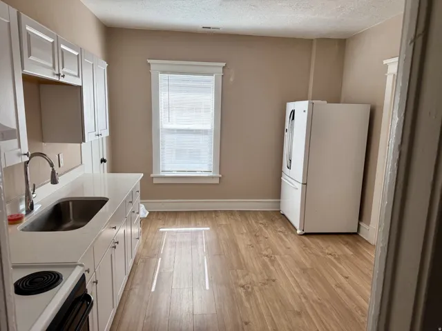 Kitchen featuring white shaker cabinetry, an integrated stainless steel sink, a modern pull-down faucet, wood-finish flooring, and a window with blinds