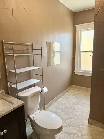 Bathroom featuring a white toilet, dark wood-finish vanity with a light speckled countertop, and a white rectangular sink