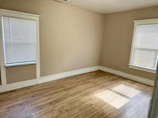 Room featuring wood-finish flooring, two windows with blinds, light-toned wall paint, and white trim molding
