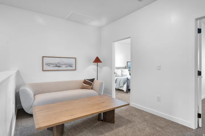 Carpeted area with white walls and trim, featuring a square ceiling access panel and a doorway leading to another room