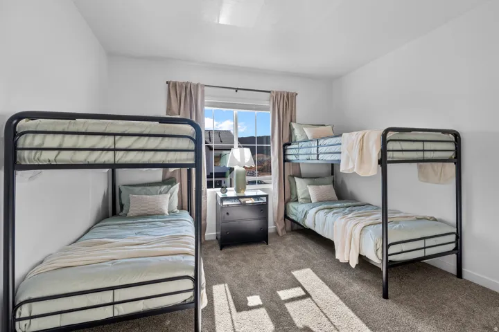 Carpeted room featuring two black metal bunk beds, a window with beige drapes, and a dresser