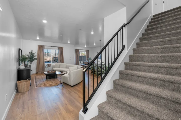 Carpeted staircase with black metal balusters and a white handrail, complemented by wood-finish flooring in the living area