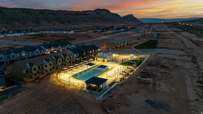 Community amenities featuring an illuminated swimming pool, shaded lounge areas, a manicured green space, and surrounding residential structures with mountain scenery