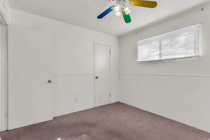 Room featuring neutral carpet flooring, white walls with wainscoting, and a window with horizontal blinds