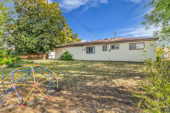 Expansive backyard featuring a partial fence, mature trees, and a siding exterior