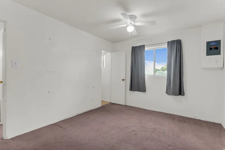 Carpeted room featuring a ceiling fan with integrated lighting, a window providing natural light, and a white electrical panel