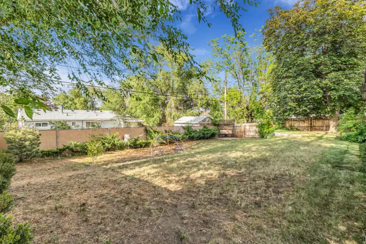 Expansive rear yard featuring mature trees, partial wood fencing, and a chain-link fence