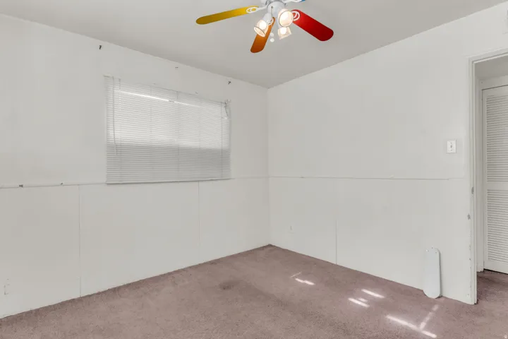 Room featuring a window with blinds, a ceiling fan with integrated lighting, and wall paneling