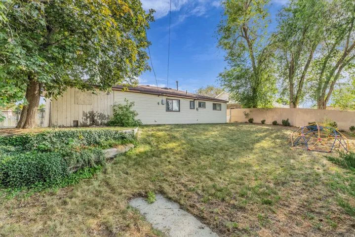 Expansive backyard featuring a partial stucco wall, mature trees, and an elevated planting area with established ground cover