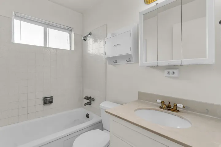 Bathroom featuring a vanity with an oval undermount sink, brass-finish faucet, and light-toned countertop