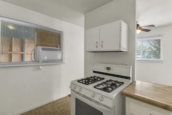 White gas range with four burners, integrated oven, and overhead cabinetry