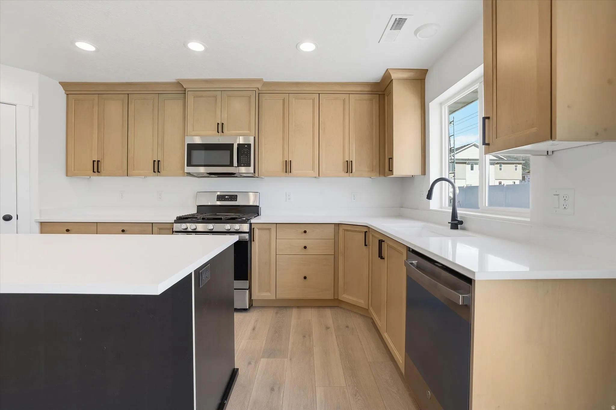 Modern kitchen featuring light wood-finish cabinetry, stainless steel appliances, and white countertops