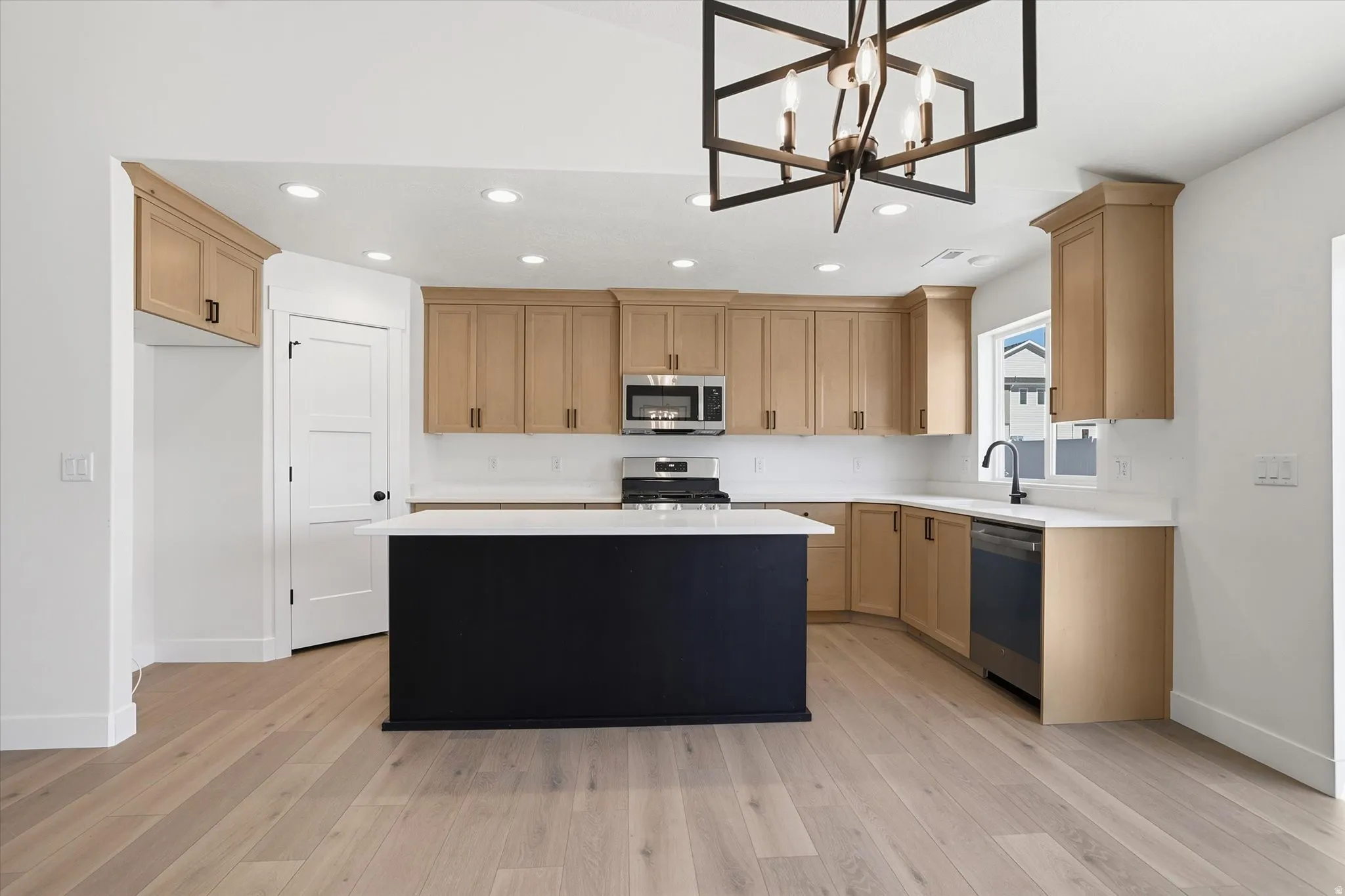 Modern kitchen featuring light wood-finish cabinetry, white countertops, and stainless steel appliances