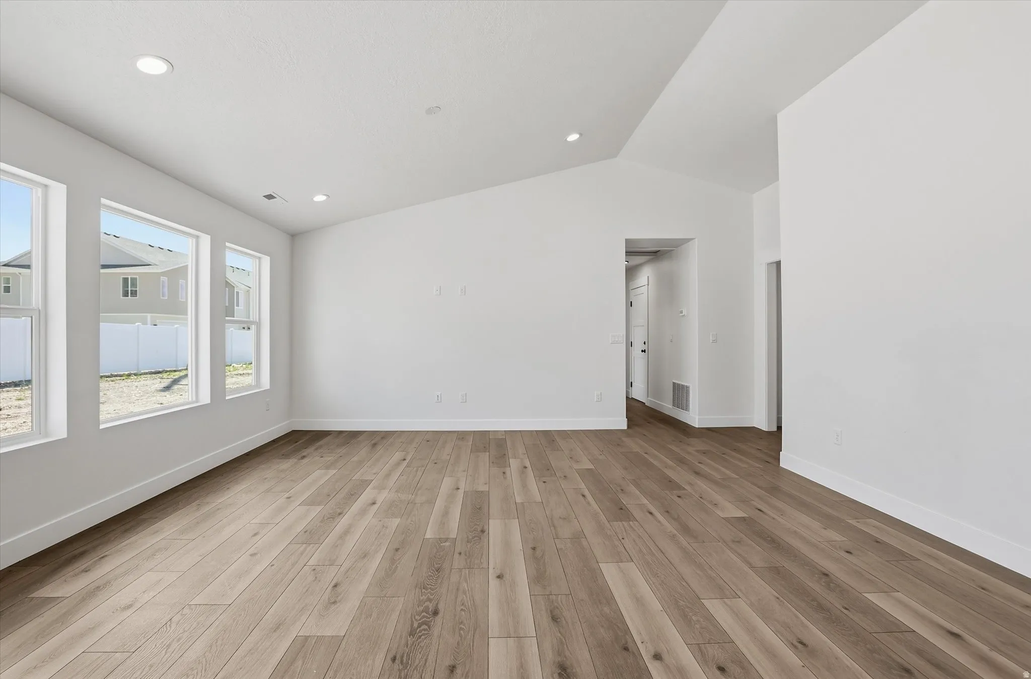 Spacious room featuring wood-finish flooring, abundant natural light from multiple windows, recessed ceiling lighting, a vaulted ceiling, and white baseboards