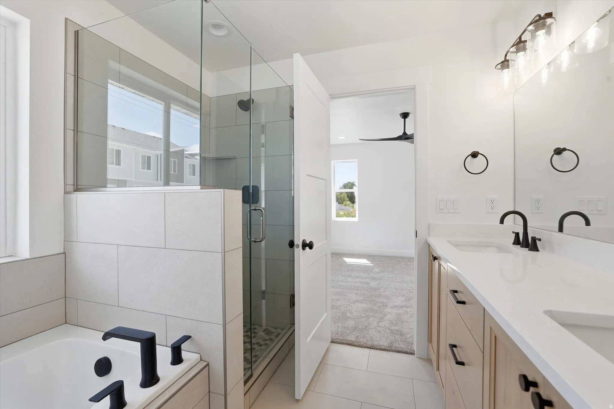 Modern bathroom featuring a dual vanity with light wood cabinetry, white countertops, and matte black fixtures