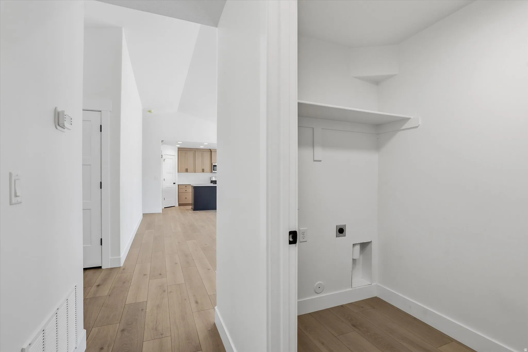 Dedicated utility closet with a built-in shelf, washer/dryer hookups, and wood-finish flooring