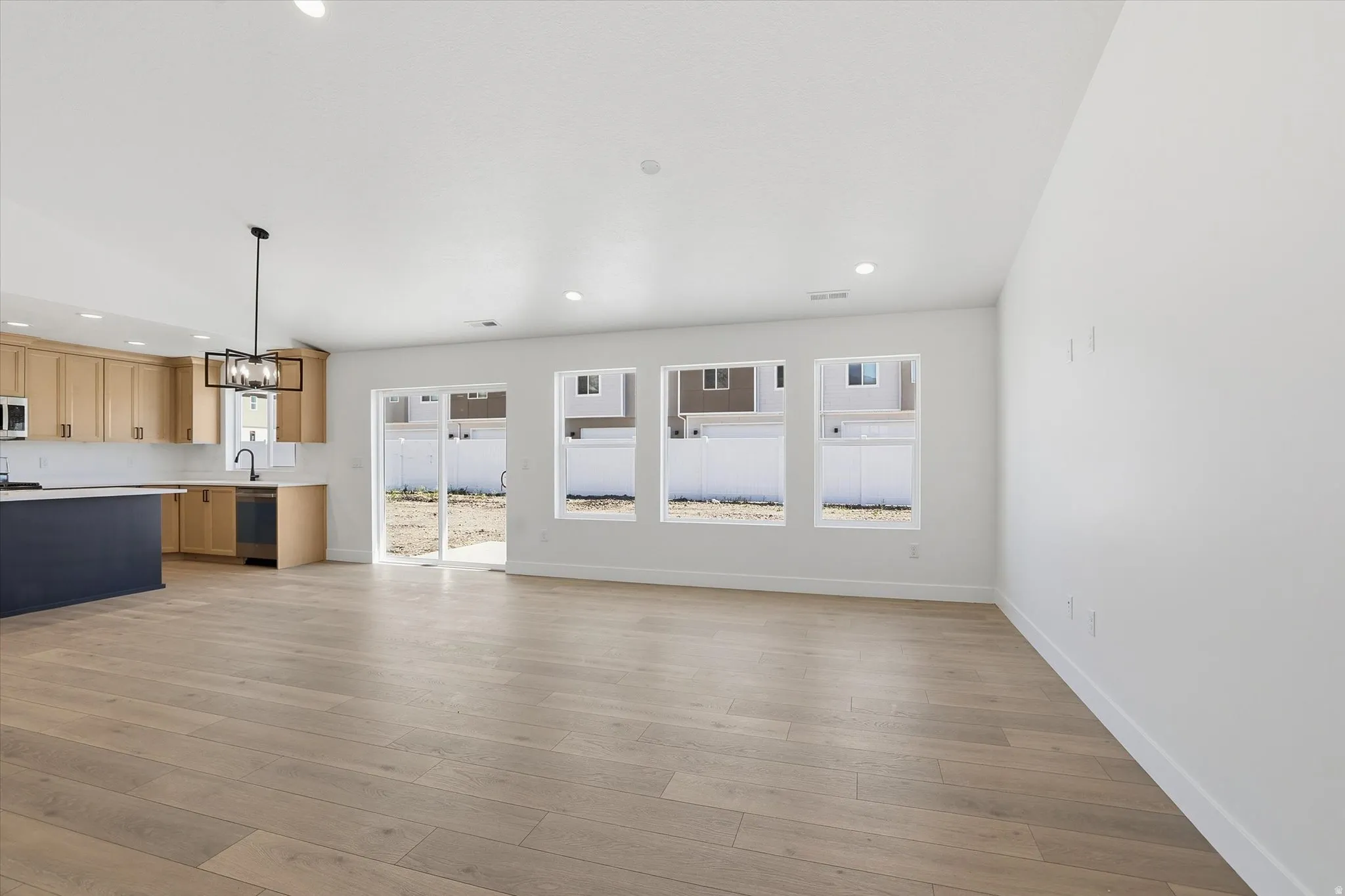 Open-concept living area featuring light wood-finish flooring, recessed lighting, and a contemporary chandelier