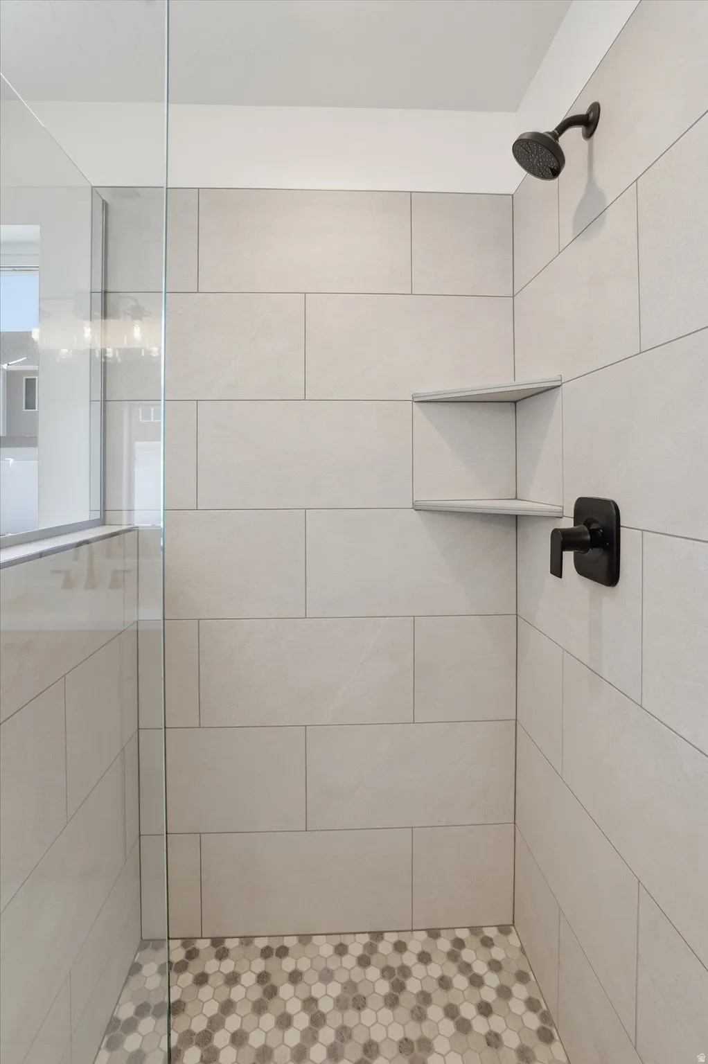 Shower enclosure featuring large format light-toned wall tiling, contrasting hexagonal mosaic floor tiling, and a built-in shower niche