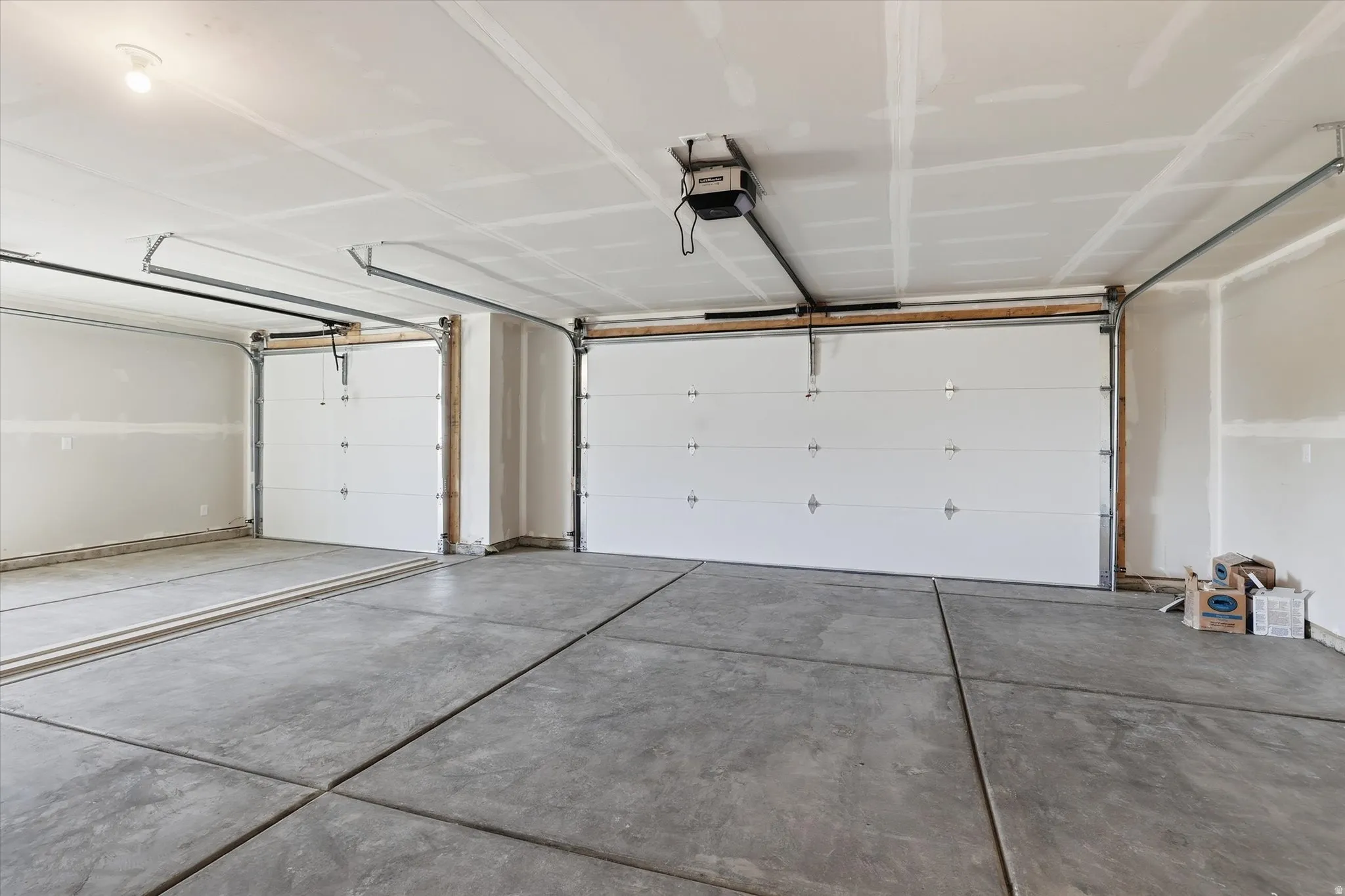 Spacious two-car garage featuring concrete flooring, unpainted drywall, two overhead garage doors, and an exposed ceiling light fixture