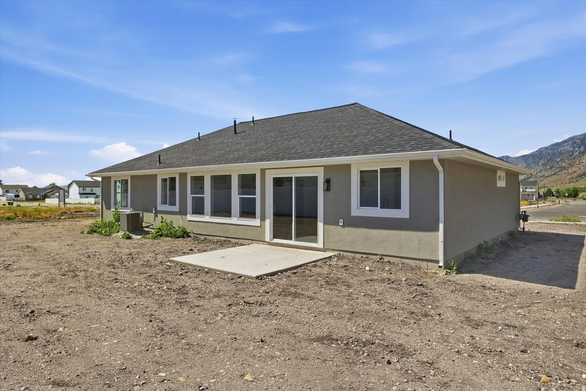 Rear exterior featuring a concrete patio, multiple windows with white trim, and a sliding glass door