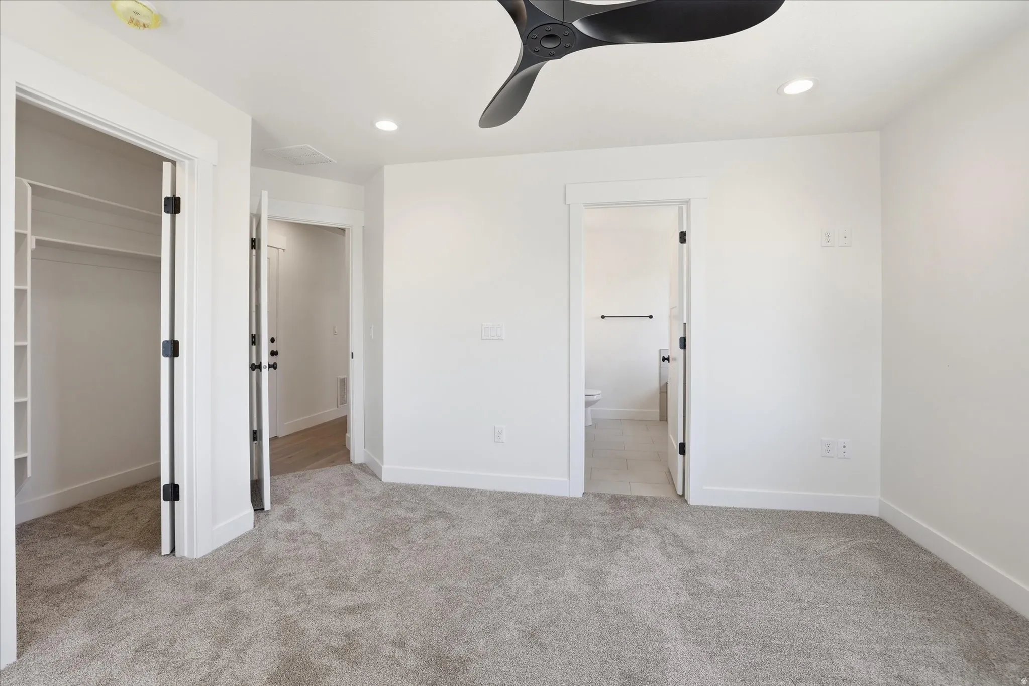 Spacious interior room featuring light gray carpeting, crisp white walls, a contemporary black ceiling fan, recessed lighting, and white baseboards