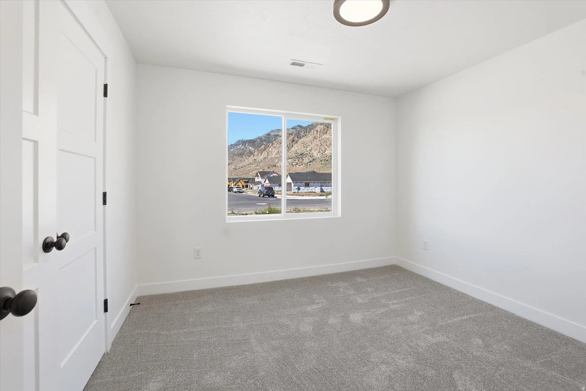Bright room featuring a window overlooking a mountainous landscape, a white paneled door with dark hardware, gray carpet, and a ceiling-mounted light fixture