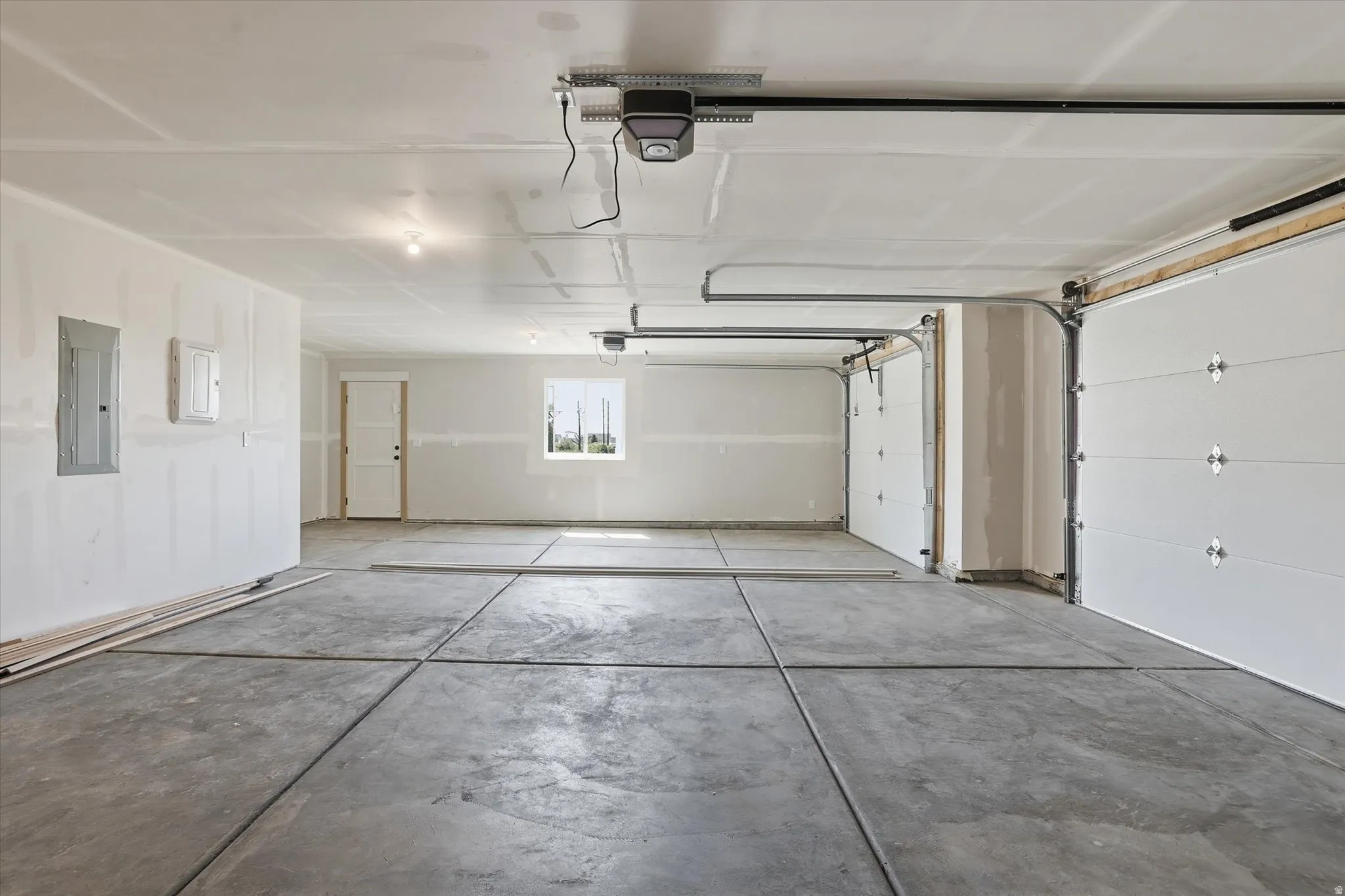 Spacious three-car garage featuring a concrete floor, three overhead garage doors with automatic openers, a rear access door, and a single window allowing natural light