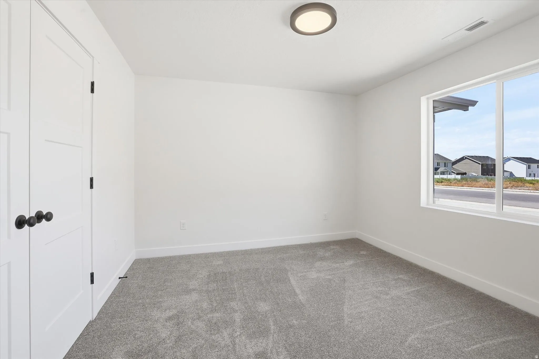 Neutral-toned room featuring a large window, white walls, and gray carpet