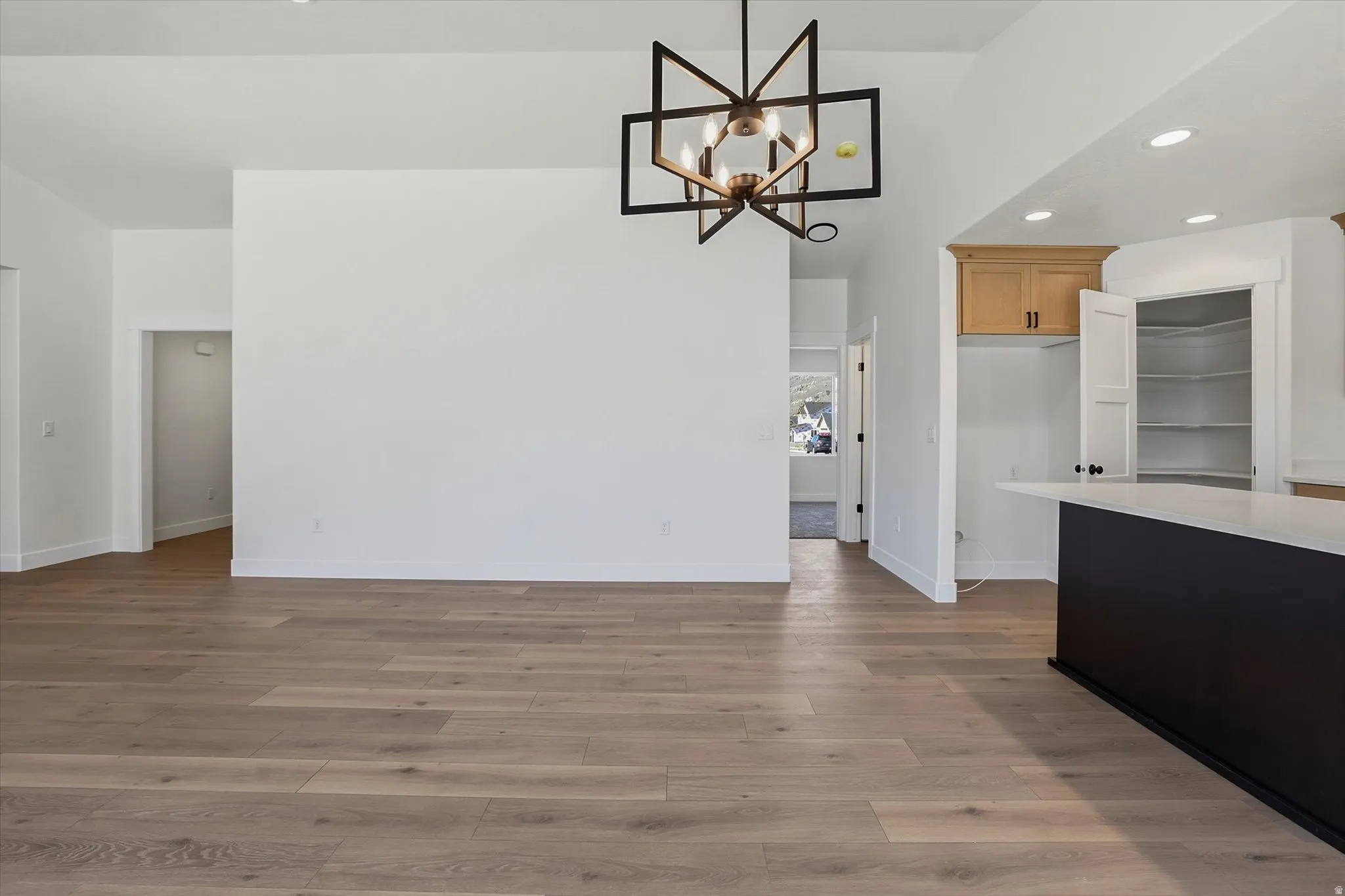 Spacious interior featuring wood-finish flooring, a contemporary chandelier, vaulted ceilings, a kitchen island with a light-toned countertop, and a built-in pantry with shelving