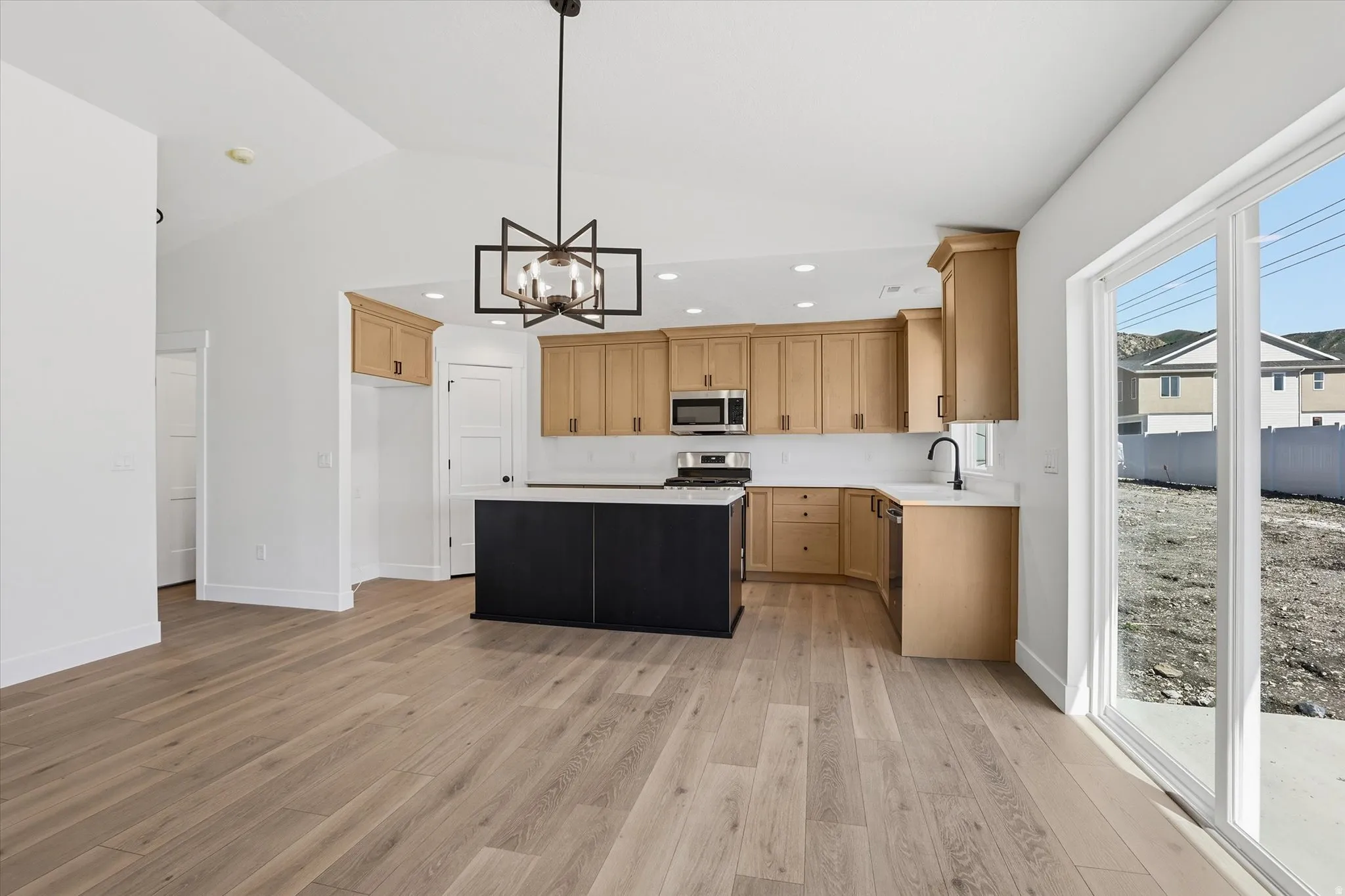 Open-concept kitchen and living area featuring vaulted ceilings, wide plank wood-finish flooring, a kitchen island with dark cabinetry, light wood-finish perimeter cabinetry, and sliding glass doors