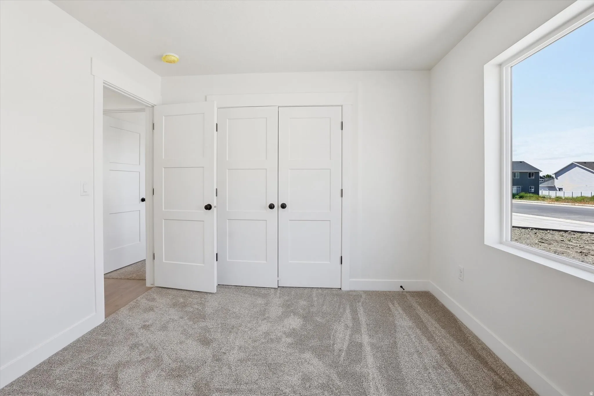 Carpeted room featuring a large window, white trim, and white three-panel interior doors with matte black hardware