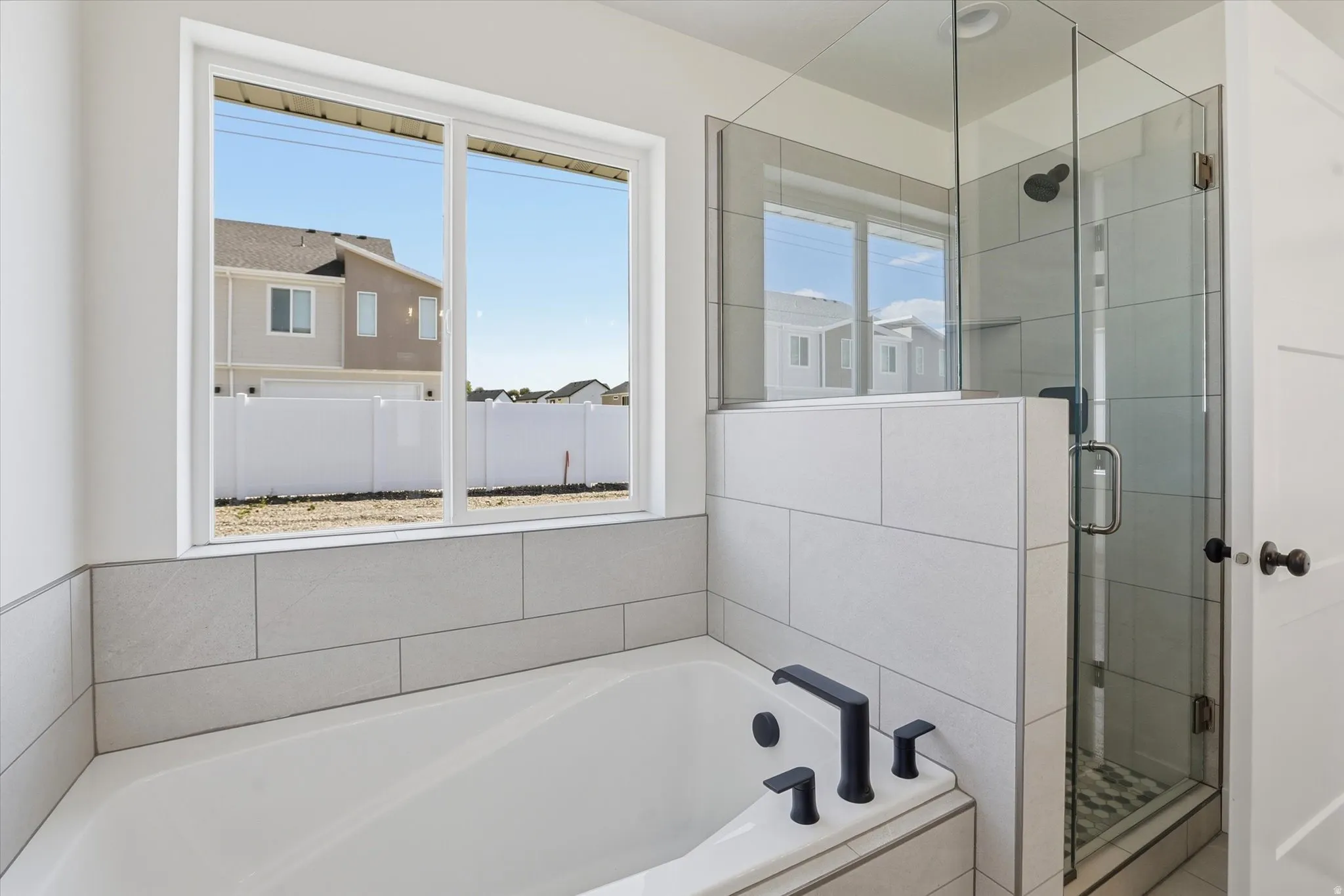 Bathroom featuring a built-in tub with matte black fixtures, a tiled surround, and a clear glass shower enclosure