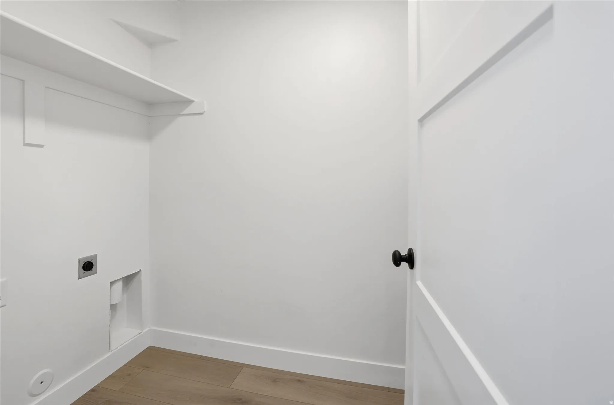 Dedicated utility space featuring built-in shelving, wood-finish flooring, and a modern interior door with a matte black knob